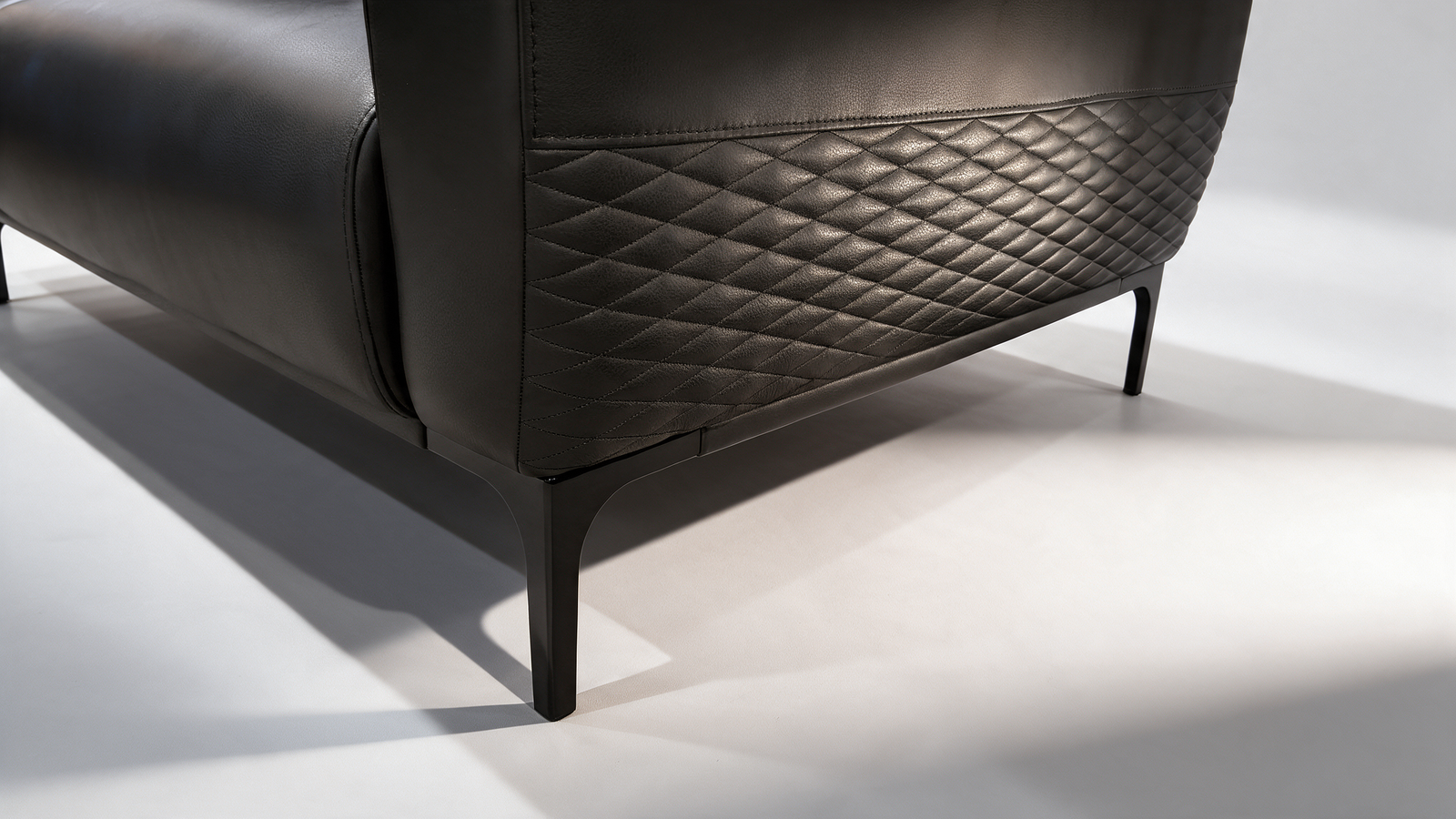 Quilted diamond-stitch back detail on black faux leather sofa