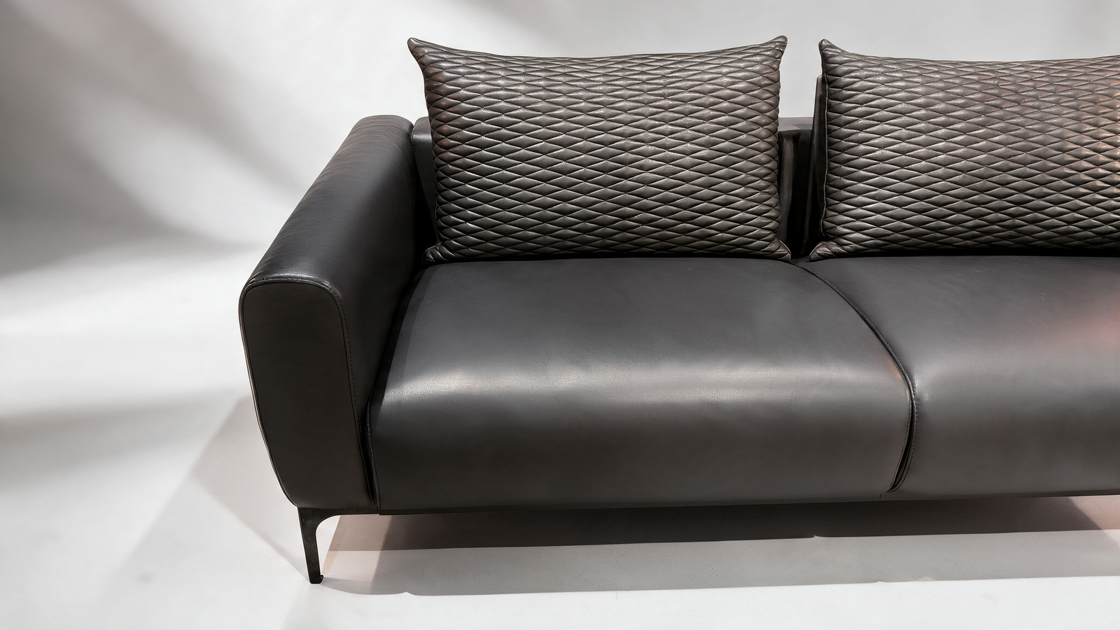 Black faux leather sofa with quilted cushions, angled view
